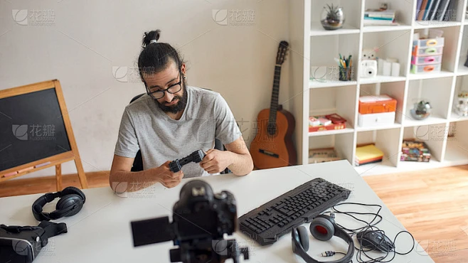 戴眼镜的男性科技博主看着游戏控制杆，一边拿着它一边录制关于家里新设备的视频博客或视频博客