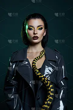美女蟒蛇黄蛇在她的脖子上乳胶闪亮的雨衣。女孩肩上的黄蛇。美黄色眼影妆，深紫红色唇膏