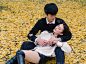 一个年轻的中国男子坐在铺满金色银杏叶的地上，怀里抱着他美丽的女友，秋像概念，情人概念。