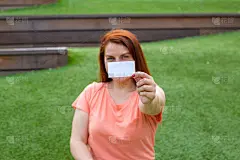 幸福美丽的姜女人拿着白色的卡片孤立在绿色的背景。幸福的情感。坐在公园长椅上的女孩。