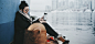 Woman sitting by a snowy city lake in boots, scarf, with leather tote.