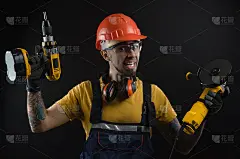 一个年轻人在黑色背景下摆姿势，穿着工作服和一个建筑工具
