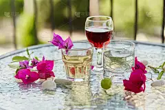 夏日明亮的鸡尾酒，一杯红酒，粉红色的九重葛花用鹅卵石装饰。夏日壁纸近了