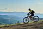 Cyclist man riding electric mountain bike outdoors along grassy trail in the mountains. Cyclist man riding electric mountain bike outdoors. Male tourist biking along grassy trail in the mountains, wearing helmet and backpack. Concept of sport, active leis