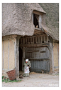 This may contain: an old woman is standing in front of a thatched house with a broom and bucket
