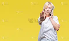年轻美丽的金发女人打电话和谈论智能手机在孤立的背景与开放的手做停止标志，严肃和自信的表情，防御手势
