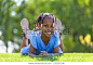 Outdoor portrait of a cute young black girl  lying down on the grass and smiling - African people