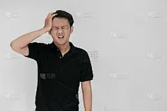 肖像的年轻亚洲男子孤立在灰色背景遭受严重的头痛，按压手指太阳穴，闭上眼睛以缓解痛苦无助的面部表情。