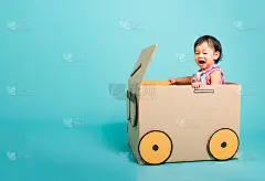 快乐亚洲宝贝女孩在开车玩车时的微笑创意由纸箱想象，暑期旅游概念，工作室拍摄在蓝色背景与文本复制空间