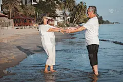 这对浪漫的亚洲老年情侣站在夏日海滩上的夕阳下跳舞。退休后的度假和夏季旅游休闲活动的概念