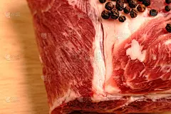 一块木板上放着红肉和胡椒球。可见的脂肪层和肉的质地。猪肉