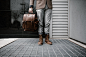 Photo of Man in Brown Blazer,Gray Pants, and Brown Boots Holding Brown Leather Bag Standing Outside Building