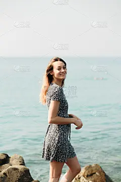 一个年轻美丽的女孩穿着大石头，风景如画的海边