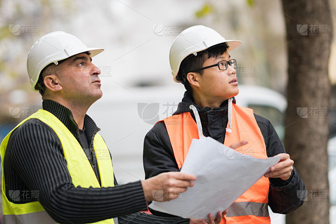 年轻的亚洲学徒在建筑工地与资深工程师工作。在户外