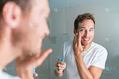 微笑的年轻人把面霜在眼睛下治疗皱纹或眼袋，抗衰老的面部治疗。男性美