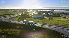 带货运拖车的白色半挂车通过高速公路立交桥鸟瞰图。十八惠勒是新的，装载仓库在背景中看到。