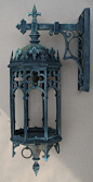 This may contain: an ornate blue metal wall light hanging from the side of a white wall with crosses on it