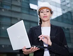 微笑的女工程师在西装和帽子与文件夹是探索项目在他的笔记本电脑