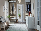 A hallway with floor-to-ceiling storage, consisting of white shelves, clothes rails and posts for storing clothes, bags and shoes. Shown together with two white chest of drawers and a bench in white stained solid birch.