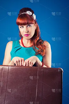 漂亮的海报女郎摆姿势与复古手提箱对抗蓝色