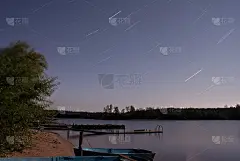 一个夏夜的风景在Seliger湖(俄罗斯)。星星的天空(星迹)，对岸的森林，水面和有船的海滩都可以看