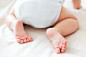 Baby's feet. little child wearing white bodysuit and diaper. cozy morning bedtime at home. Premium Photo