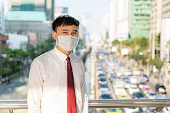 年轻的亚洲商人穿着白衬衫去污染城市工作，她戴着防护口罩，在泰国曼谷防止PM2.5粉尘、雾霾、空气污染