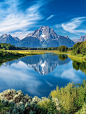 An enchanting photo of the Grand Teton National Park's Oxbow Bend, showcasing its stunning scenery with clear blue skies and reflecting water in summer. The majestic mountains reflect perfectly on mirror-like waters under the bright sunlight, surrounded b