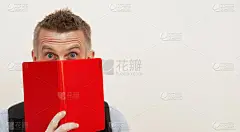 欧洲男性震惊了，把脸藏在一本红皮书后面。孤立在白色的墙壁上。本空间