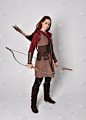 穿着中世纪棕色弓箭手服装的红头发女孩的全长肖像站着举着弓箭的姿势，与灰色的画室背景隔离.