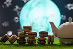 下午茶时间。茶壶和茶，在绿色的草地上，映衬着月亮和星空，还有法国甜点马卡龙。东的照片。美味的茶