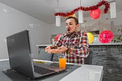 因新冠疫情的限制，一名年轻的白人男子正在家中与朋友们通过视频集体庆祝生日，正在吹生日蜡烛