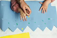 特殊教育的老师和学生穿着长袍，在桌子上用手画着生日花环和涂着丙烯颜料的黄色纸板。塑料工艺疗法。