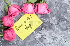 浪漫的概念。灰色的混凝土背景上，红玫瑰和刻有祝福的字母祝你有美好的一天