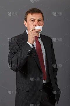 自信成熟的商人站在灰色背景前喝着咖啡