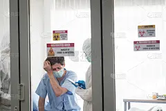 一名男性病人在控制区卧病在床。穿着防护服和口罩的医生正在检查受感染的老人。
