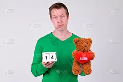 失意的年轻人拿着日历块和泰迪熊过情人节