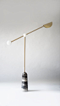 BALANCE – Floor lamp. An elegant and minimal table lamp with a rounded tapered black marble base. The brushed brass pole is connected to a central powder-coated metal ball joint. The angled pole has two light sources at either end; one in the form of an f