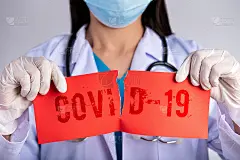 女医生戴着医用口罩、听诊器，手持写有COVID-19文字的红色撕纸。医疗保健和医疗理念。