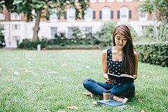 Young student readingYoung Asian student reading in public park. She's sitting on grass, with cup of coffee.
