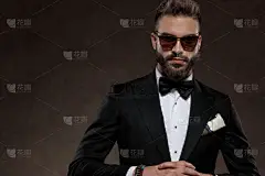 严肃的时尚新郎手拉手，戴着太阳镜，穿着西服，站在壁纸工作室的背景上问道